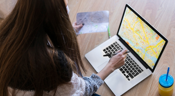 Young woman sitting on the floor looking at map on laptop